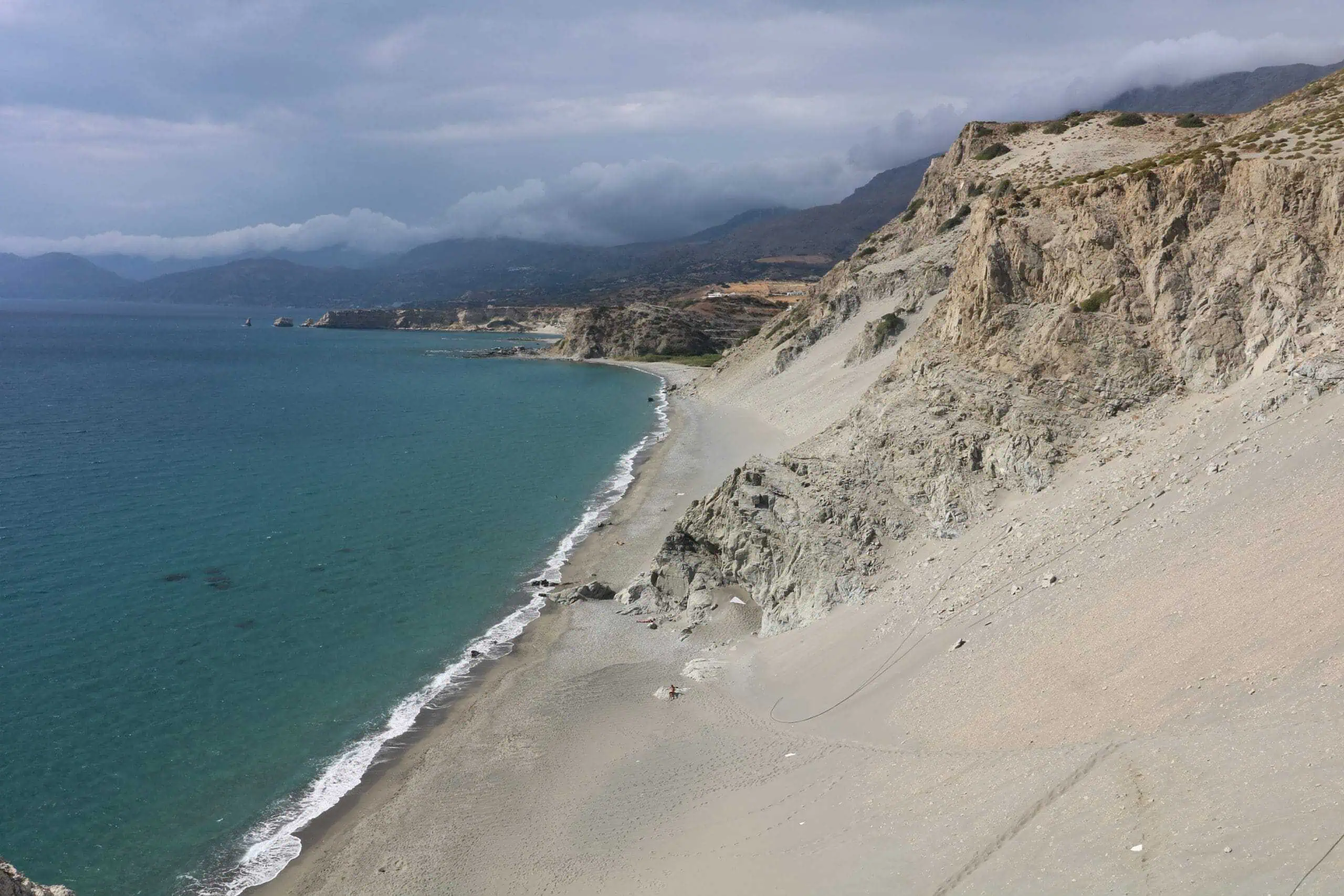 The sandy slopes of the Beach by the small town of Agios Pavlos with the rock formation that hosts the famous twin cave