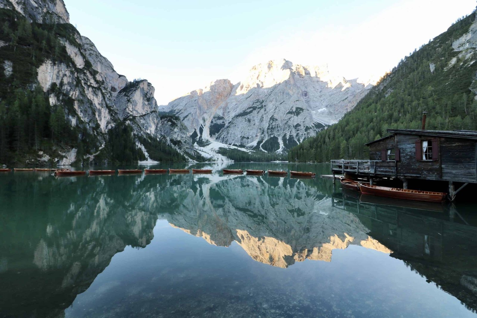 Morning glow at Lake Prags, with the rowboats lined up on the shore and the sun painting the sky in hues of orange and pink, South Tyrol, Italy