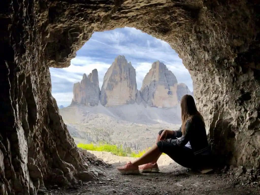 Stunning circular shaped cave with a woman sitting inside Tre Cime or Drei Zinnen in the background