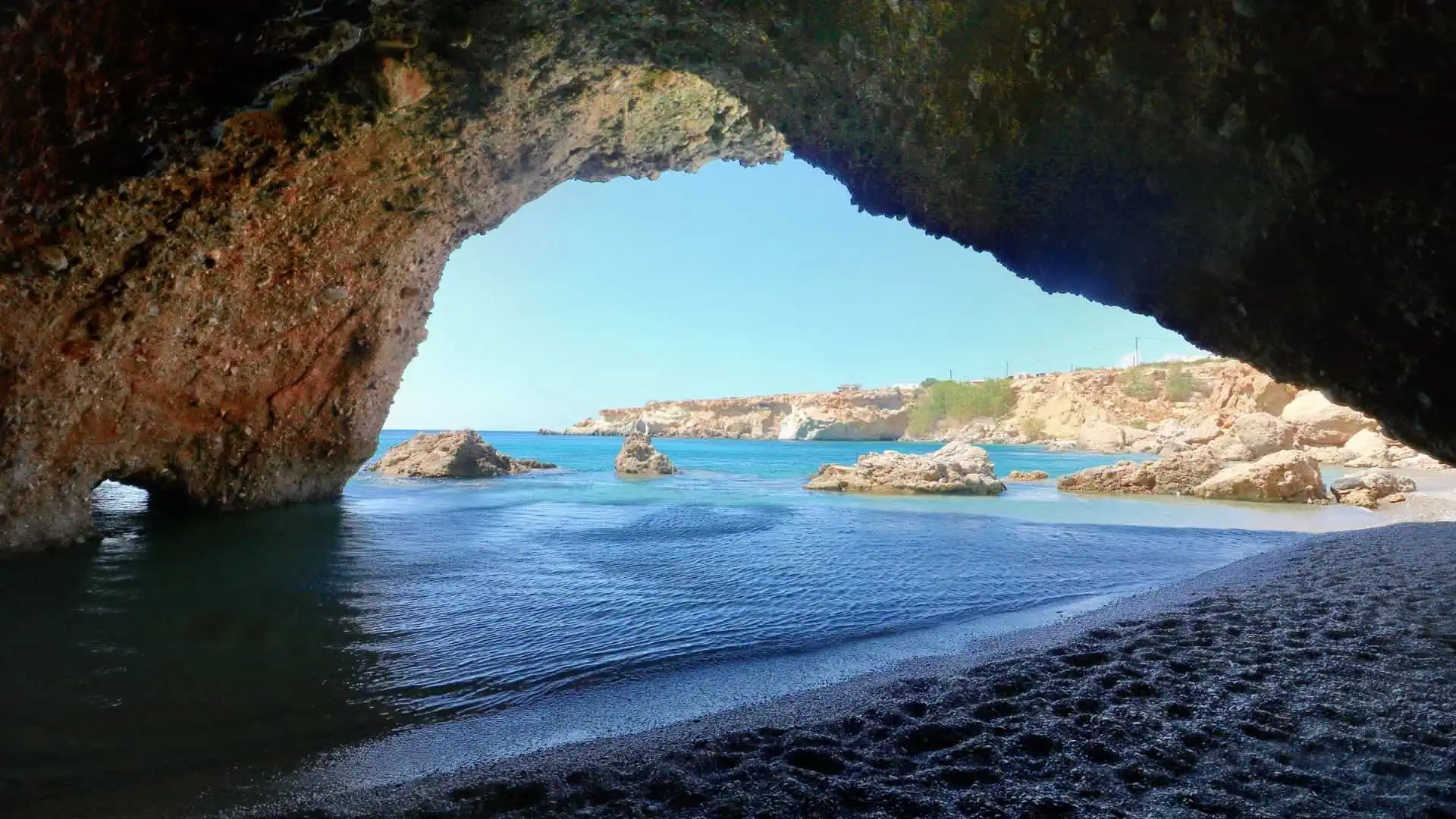 Staousa Beach Cave with some cliffs, blue sky and shallow waves in the background.