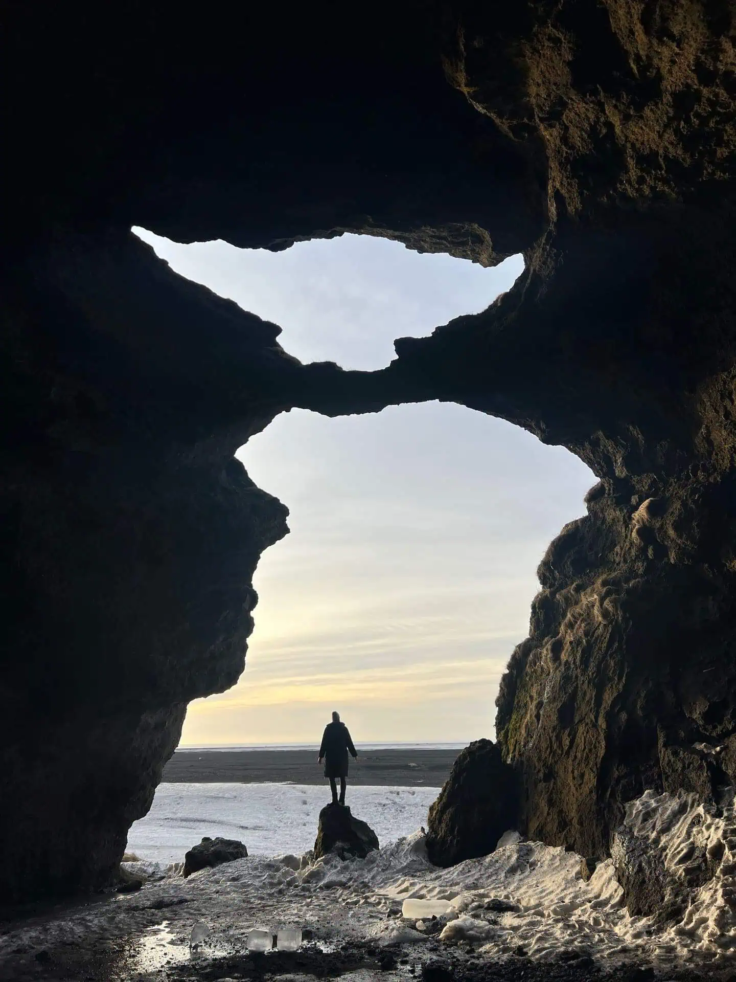 Woman standing on a rock in yoda cave with light yellowish sunrise sky in the background