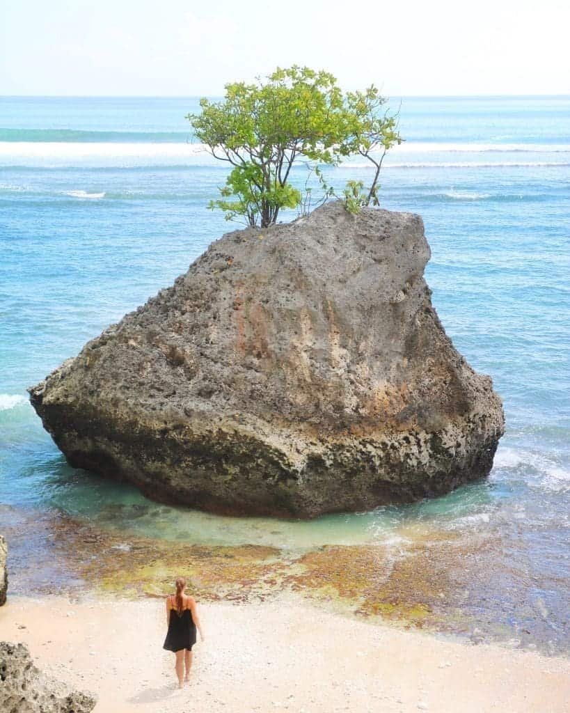 A woman standing on Bingin Beach with a large rock in the water