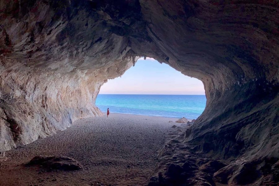 Deep Cala luna cave thit the bright eye of clear blus water and evening sky with a woman standing inside in a red dress